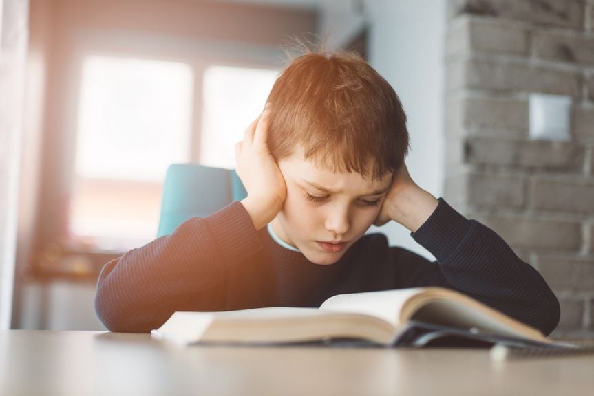 Junge liest in einem Buch und hält sich die Ohren zu