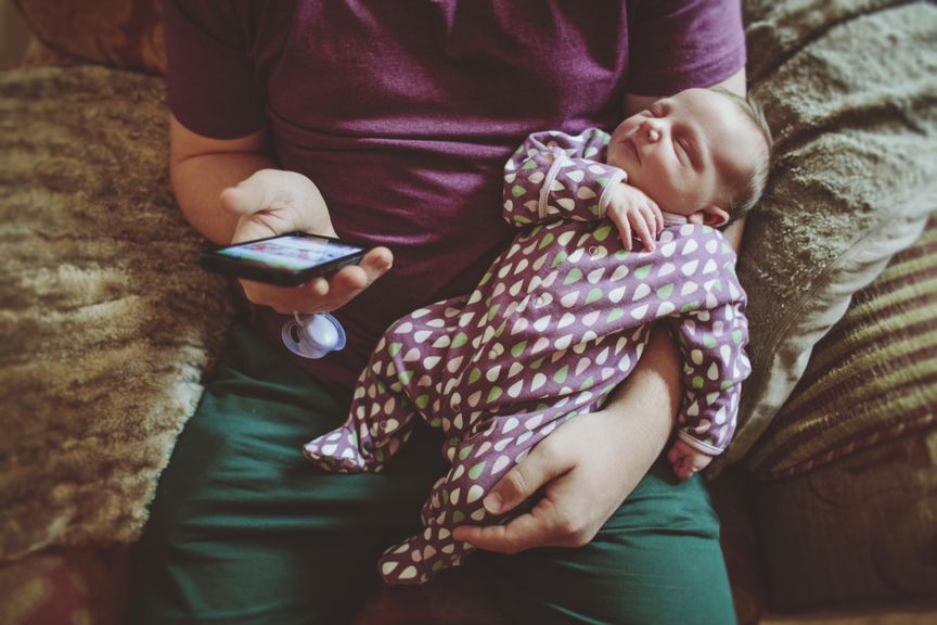 Vater mit Neugeborenem am Handy