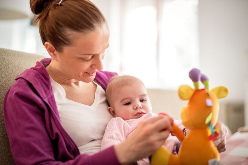 Mutter mit Baby auf dem Schoss spielt mit Stofftier