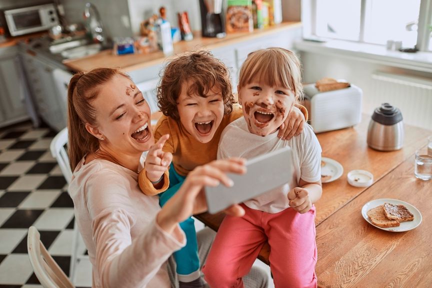 Mutter filmt sich und ihre lachenden Kinder, die auf dem Tisch sitzen mit dem Handy