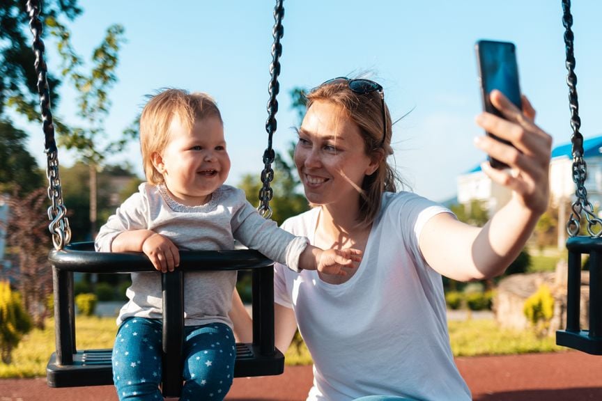 Mutter macht Foto von sich und Kind auf der Schaukel