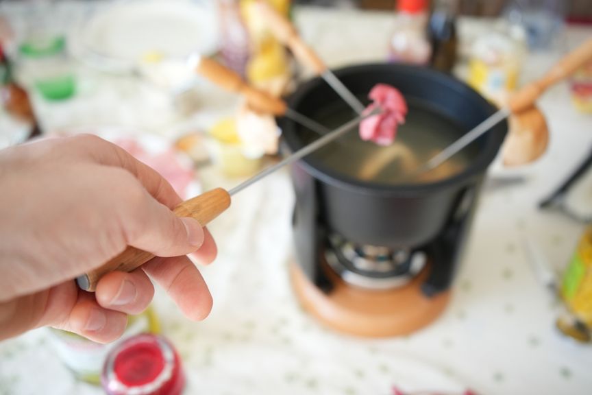 Männerhand hält eine Gabel mit Fondue-Chinoise-Fleisch