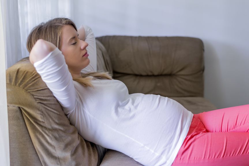 Schwangere liegt mit geschlossenen Augen auf dem Sofa
