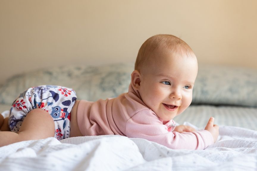 Lachendes Baby mit Stoffwindeln liegt auf dem Bauch