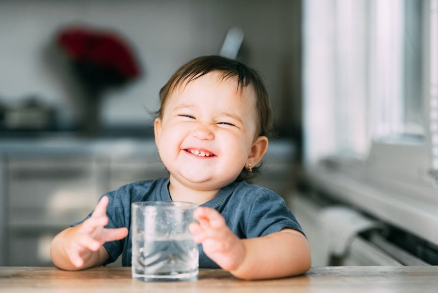 Lachendes Baby mit einem Glas Wasser