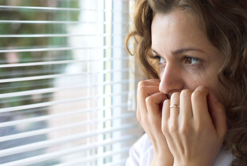 Frau blickt aus dem Fenster, Hände vor dem Mund