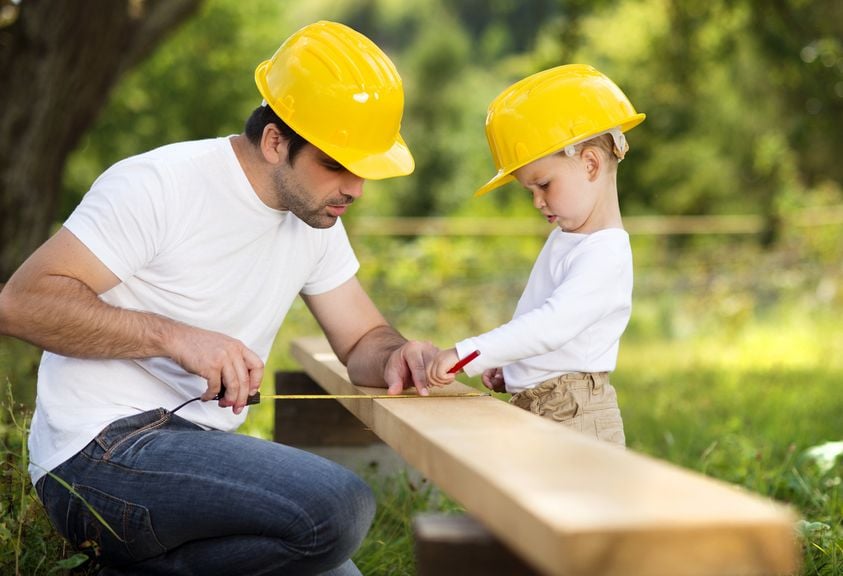 Vater und Sohn mit Schutzhelmen bei der Arbeit mit Holz