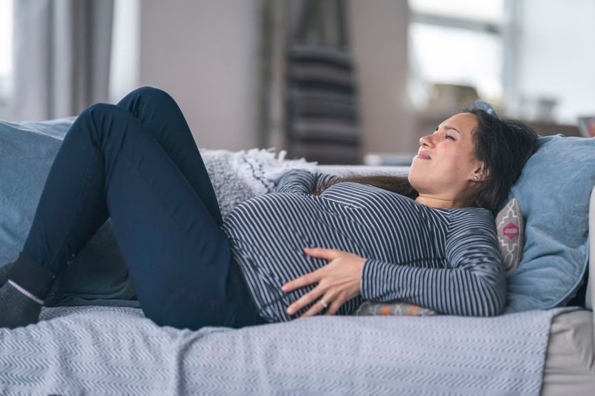 Schwangere liegt mit Schmerzen auf dem Sofa