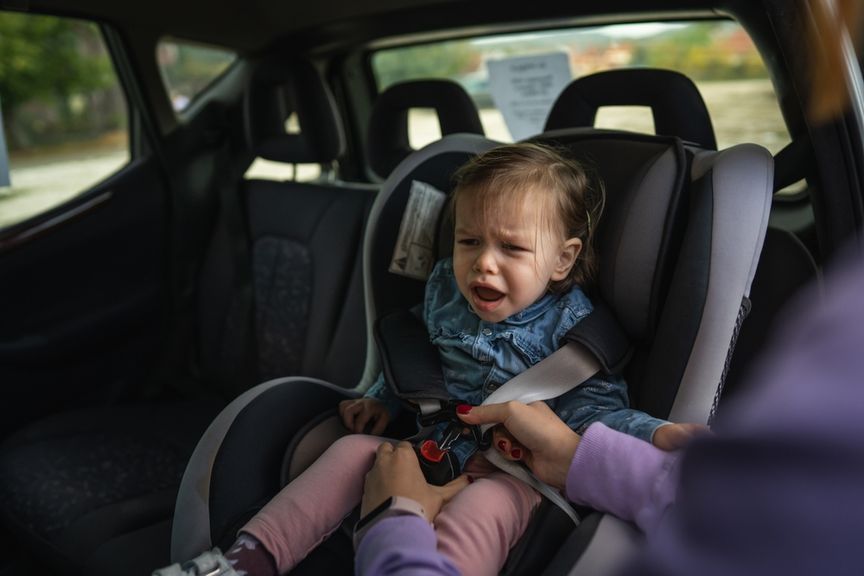 Mutter schnallt ihr protestierendes Kind im Autokindersitz an