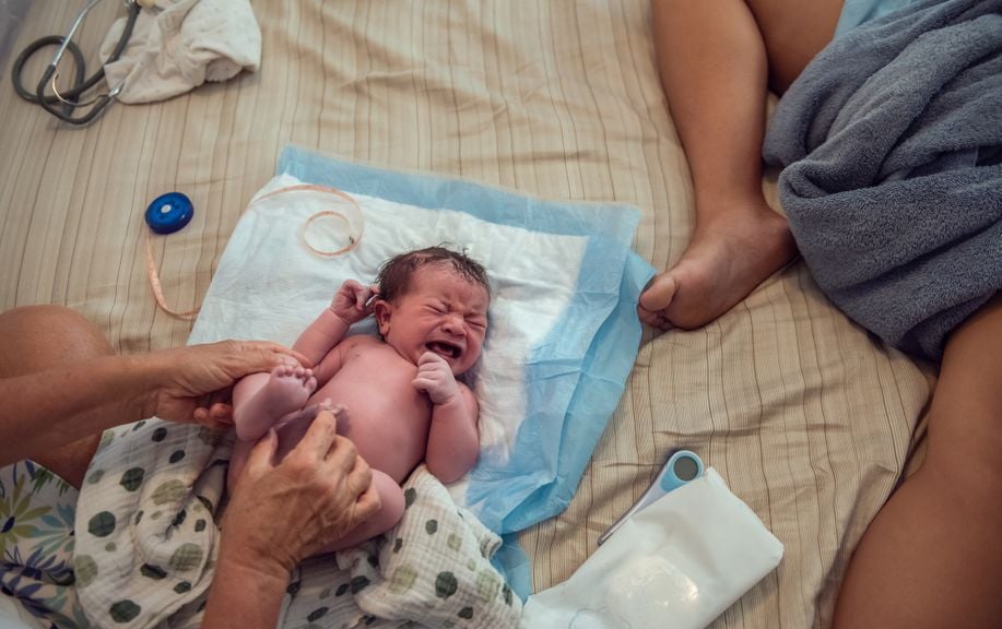 Hebamme untersucht Neugeborenes auf dem Bett