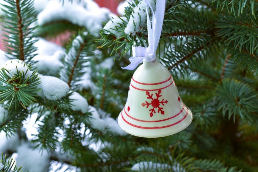 Verschneiter Weihnachtsbaum mit einer rot-weissen Glocke als Dekoration