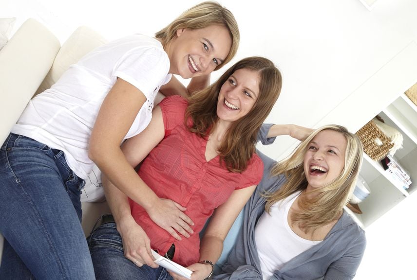 Drei lachende Frauen, eine schwanger, auf dem Sofa