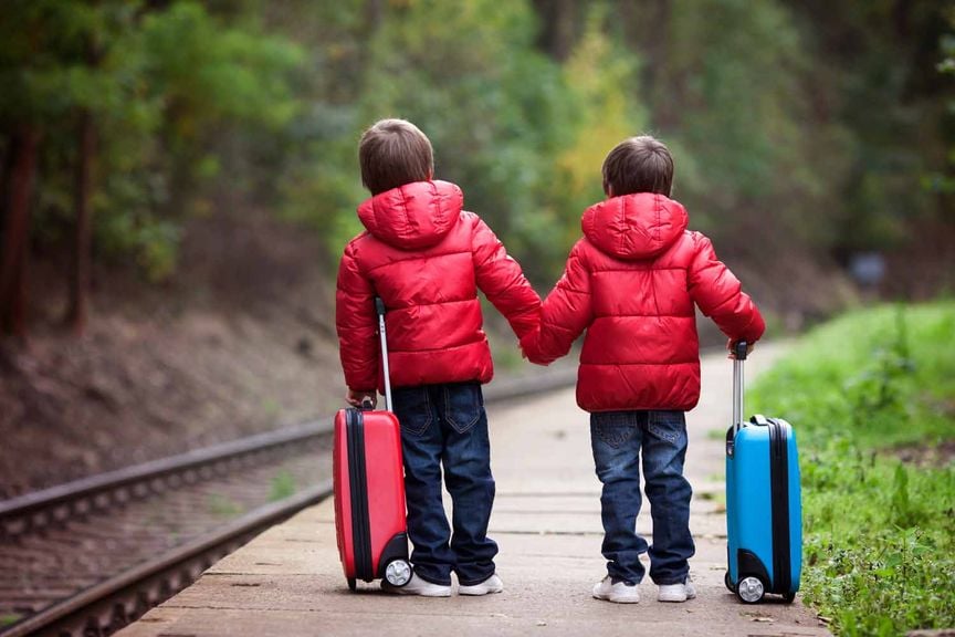 Kinder mit Koffern am Bahngleis