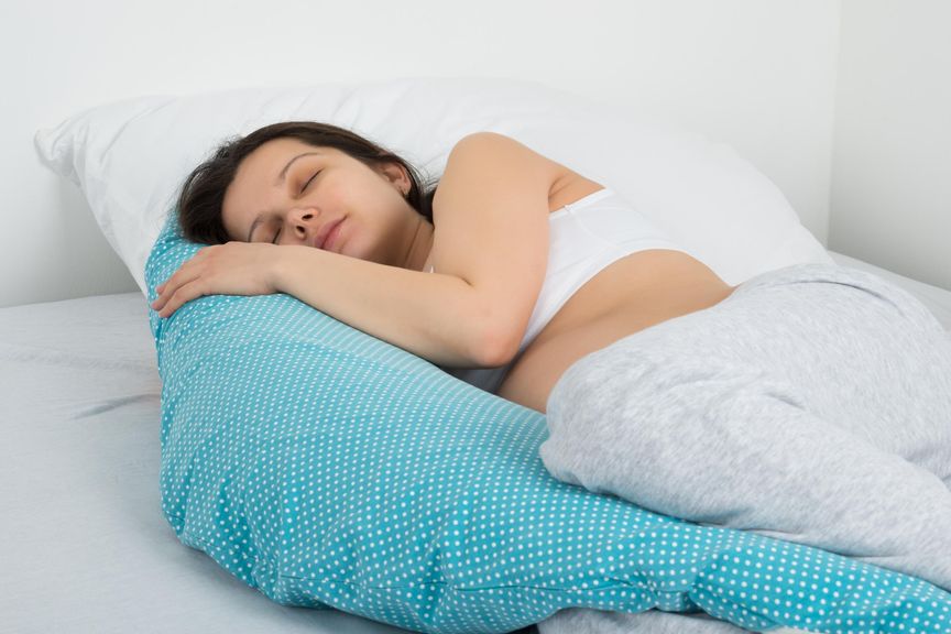 Schwangere Frau schläft in Seitenlage mit Stillkissen