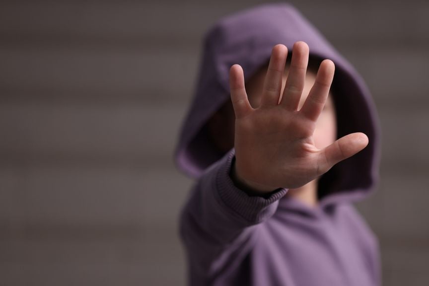 Kind im violetten Kapuzenpullover hält die Hand vors Gesicht, um "Stop" zu signalisieren