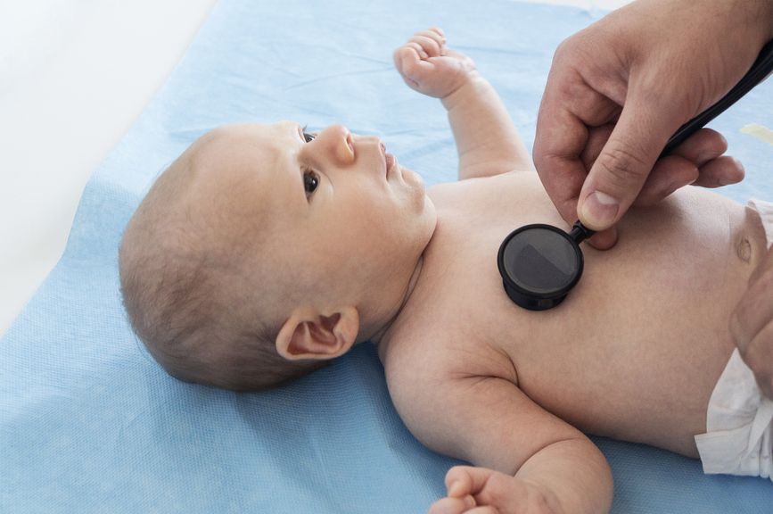 Kinderarzt hält ein Stethoskop auf der Brust eines Neugeborenen