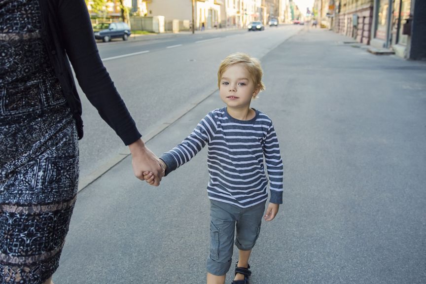 Junge an der Hand der Mutter auf dem Trottoir