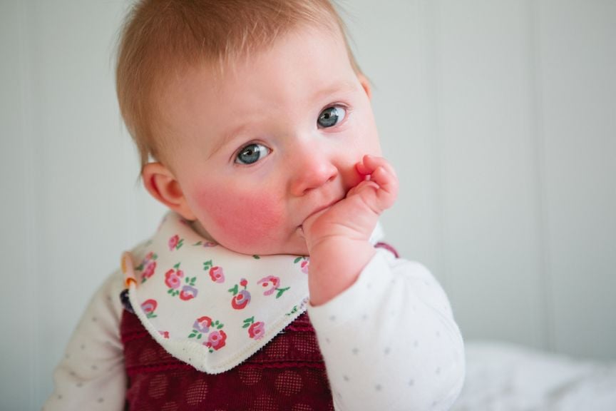 Baby mit roten Backen und Daumen im Mund