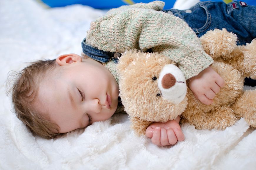 Baby schläft mit Teddy im Arm