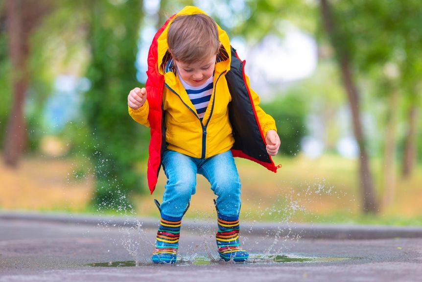 Kleinkind in Regenjacke und Gummistiefeln springt in eine Pfütze