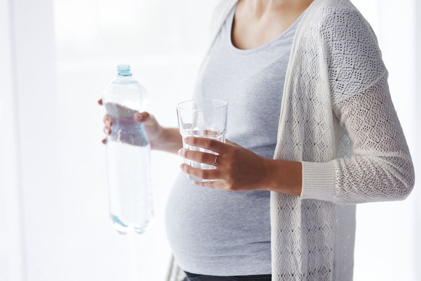 Schwangere mit Wasserflasche und Glas in der Hand
