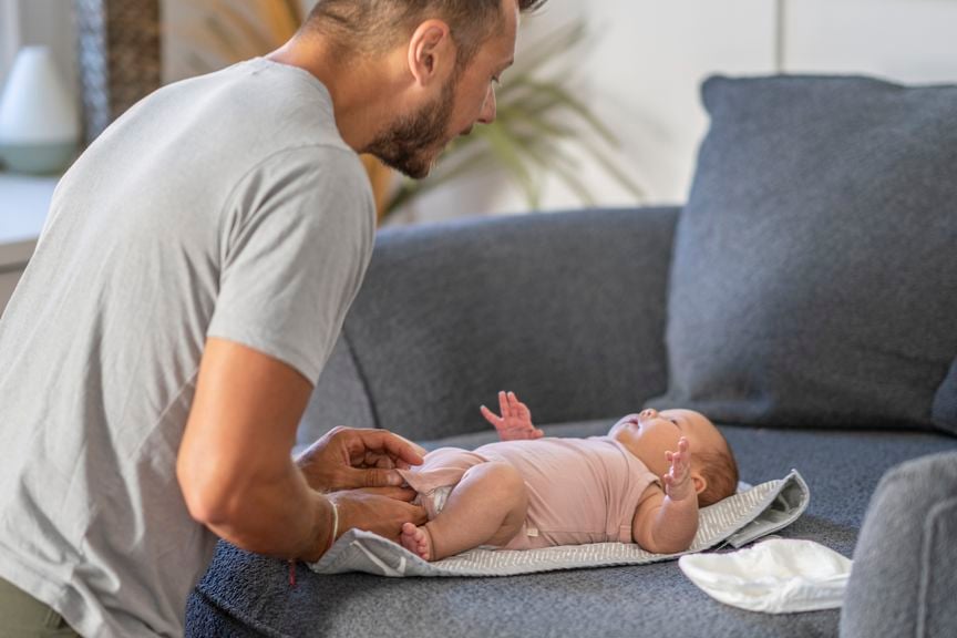 Vater wickelt Baby auf dem Sofa