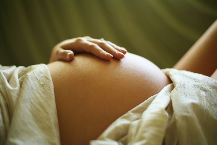 Schwangere liegt und streicht sich mit der Hand über den Bauch