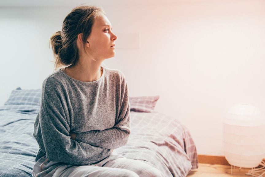 Frau mit verschränkten Armen sitzt auf dem Bett