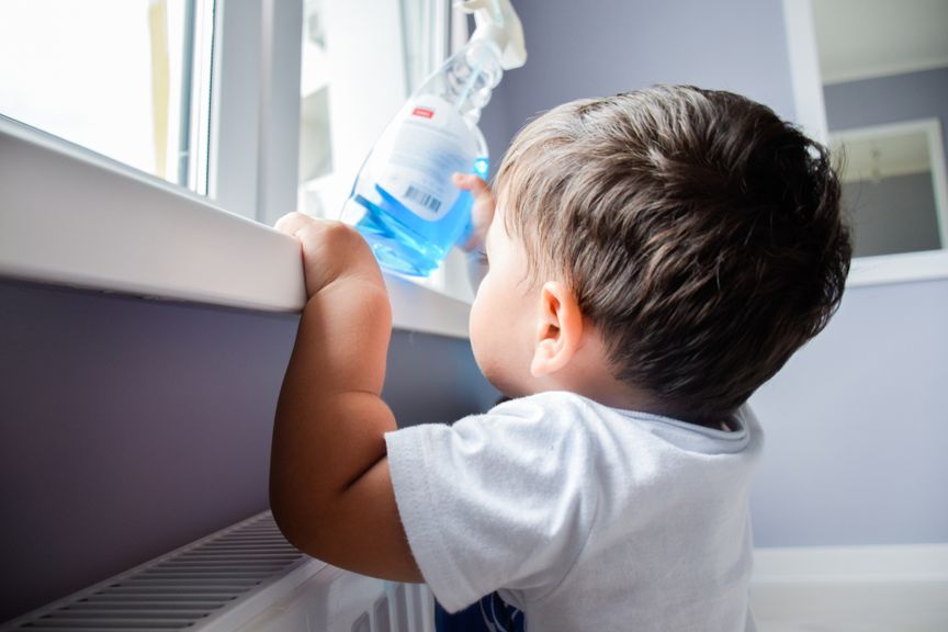 Kleinkind hält eine Sprühflasche mit Putzmittel in der Hand