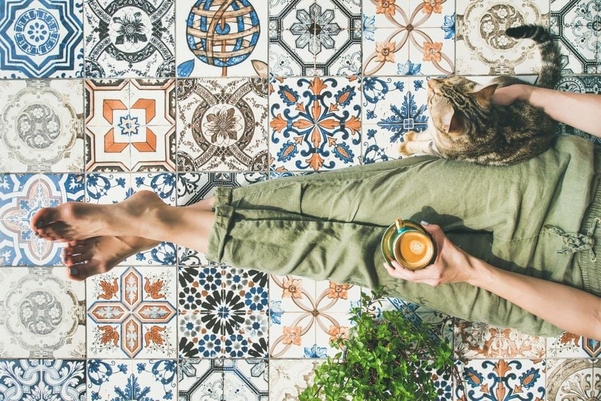 Frau mit Katze trinkt Kaffee auf dem Balkon