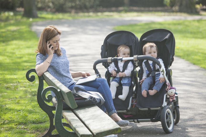 Mutter auf einer Parkbank mit Zwillingen im Buggy